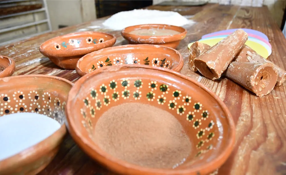 Ingredientes tradicionales para preparar muéganos de Huamantla, con piloncillo y especias en recipientes de barro