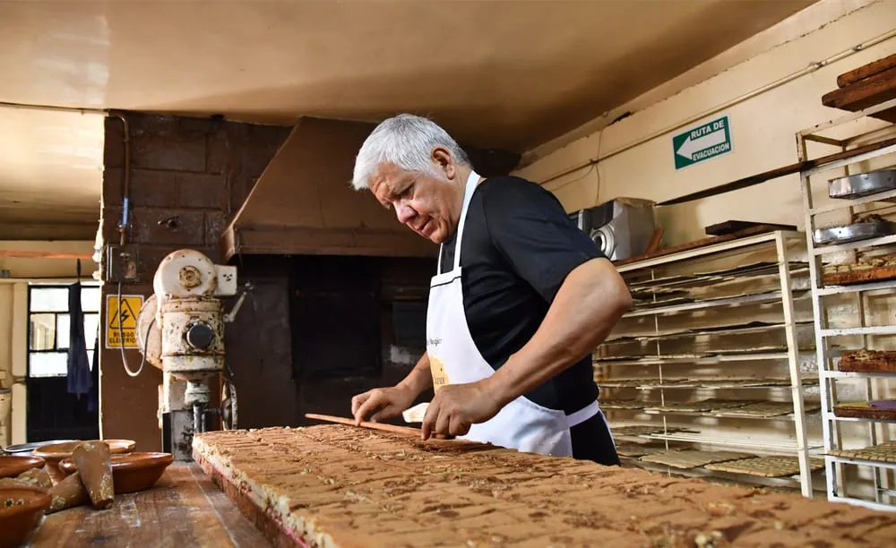 Artesano preparando muéganos de Huamantla en un obrador tradicional con charolas de producto al fondo
