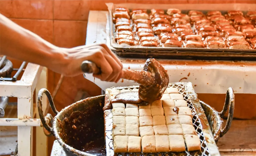 Proceso de enmielado de muéganos de Huamantla, con piezas cubiertas con miel de piloncillo y otras ya acomodadas al fondo